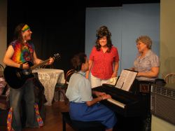 Harmony (Rodrigo Pool) plays the guitar with Lurlene on the piano (Grace Erdmann), Sara Lee (Holly Martin Czuchna), and Mama Wheelis (Sherry Bendt)
